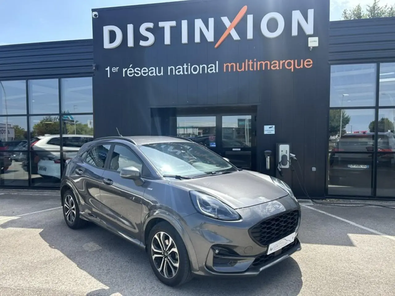 Ford Puma gris Magnetic en 3/4 avant droit avec jantes alliage et calandre noire ST-Line devant un bâtiment Distinxion.