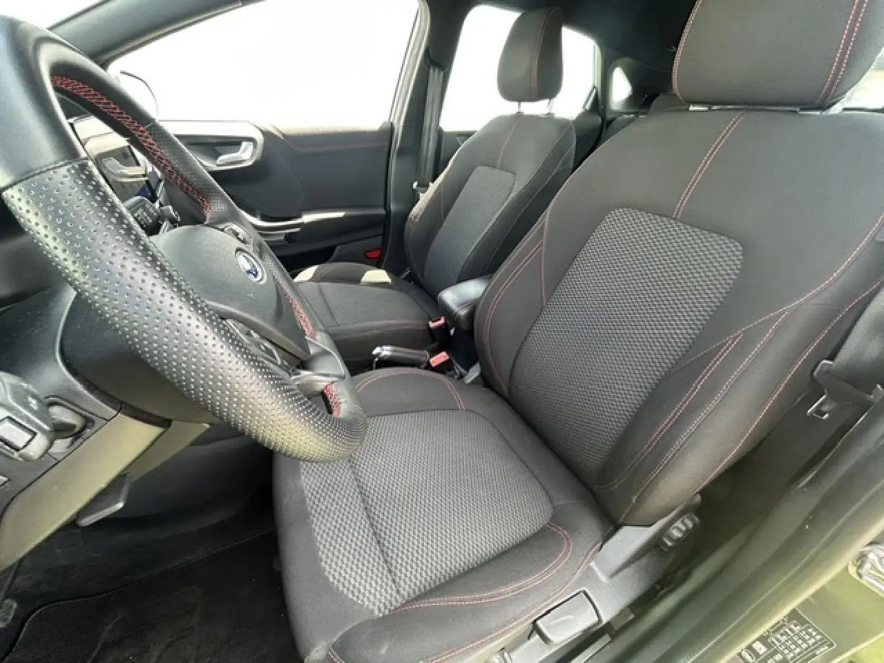 Intérieur Ford Puma ST Line 2022 vu côté conducteur, sièges tissu noir avec surpiqûres rouges et volant perforé.