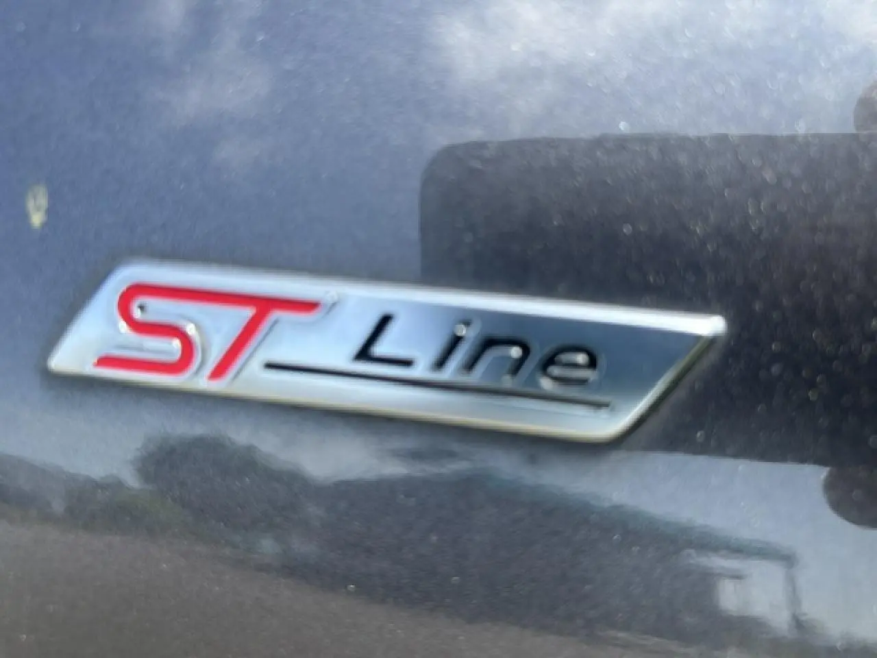 Gros plan sur le badge ST-Line rouge et noir sur la carrosserie gris magnetic d'une Ford Puma 2022.