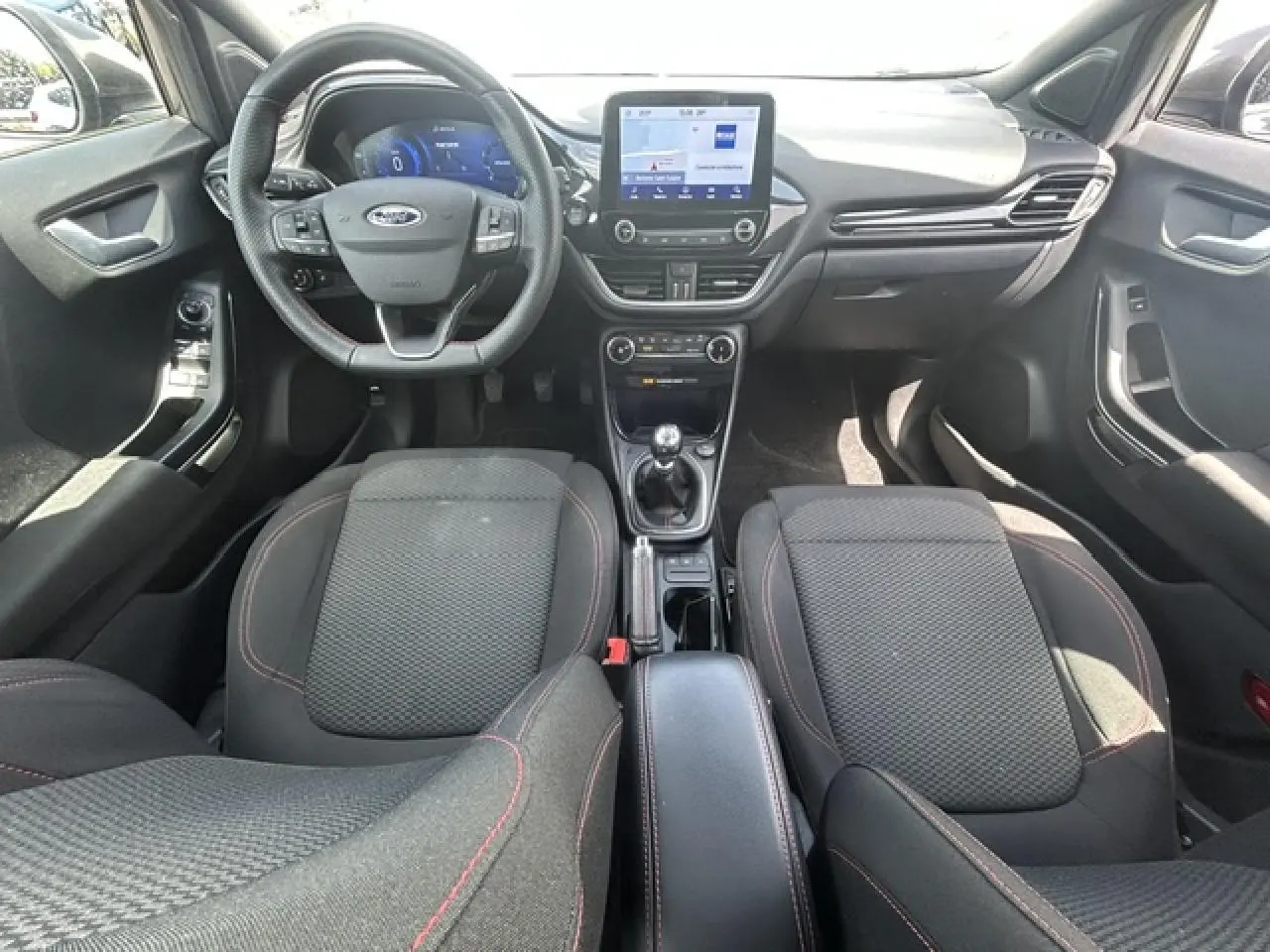 Vue intérieure avant du Ford Puma 2022 avec sièges tissu noir, volant ST-Line à méplat et écran tactile central.