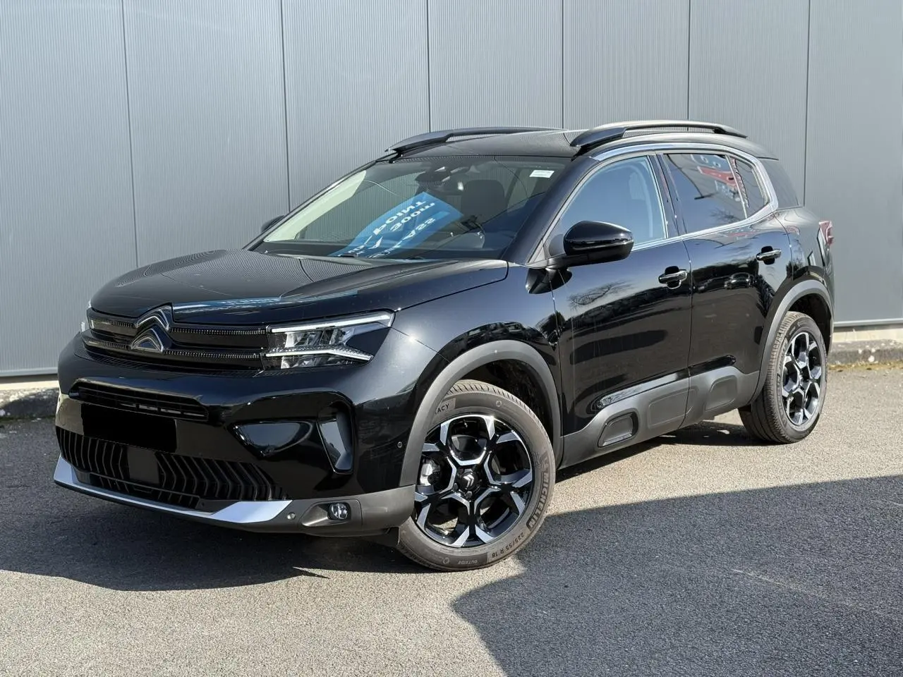 Vue 3/4 avant droit d'un Citroën C5 Aircross 2025 noir Perla avec jantes alliage bi-ton et barres de toit noires.