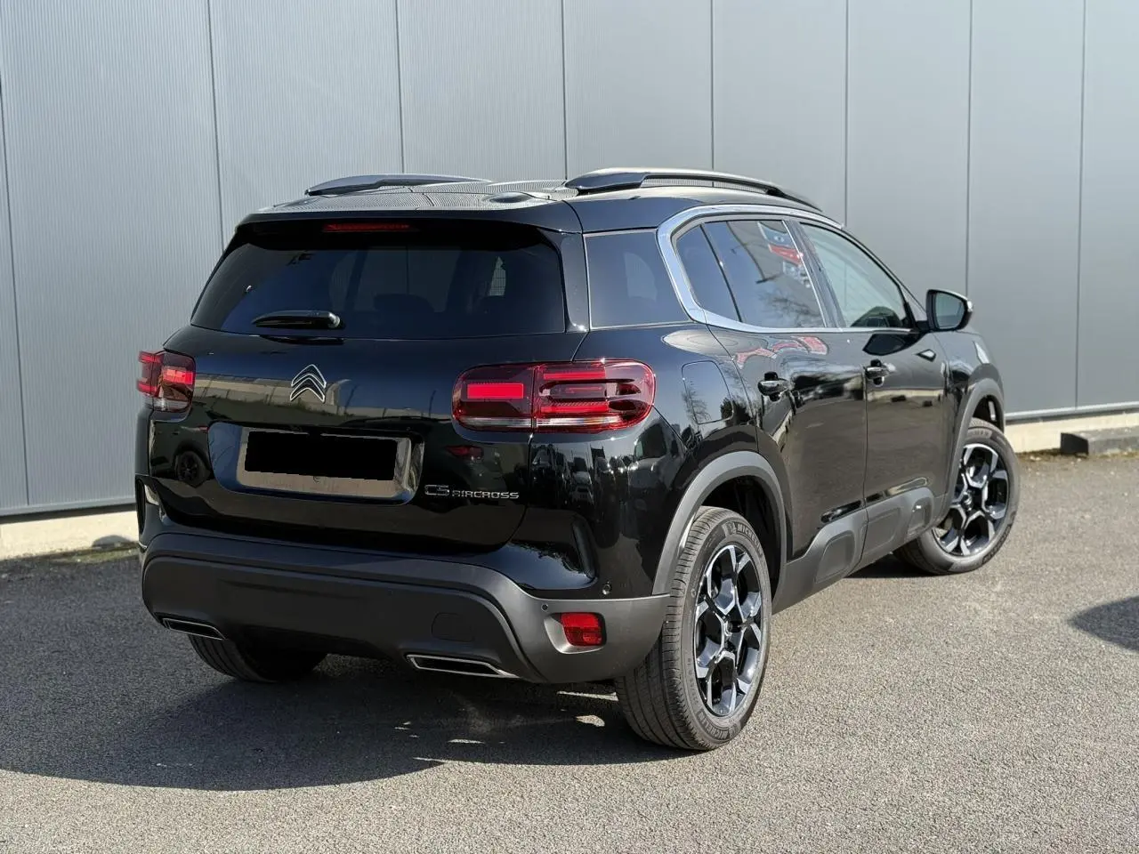 Vue 3/4 arrière droite du Citroën C5 Aircross noir Perla avec jantes alliage 18'' bi-ton et barres de toit noires.