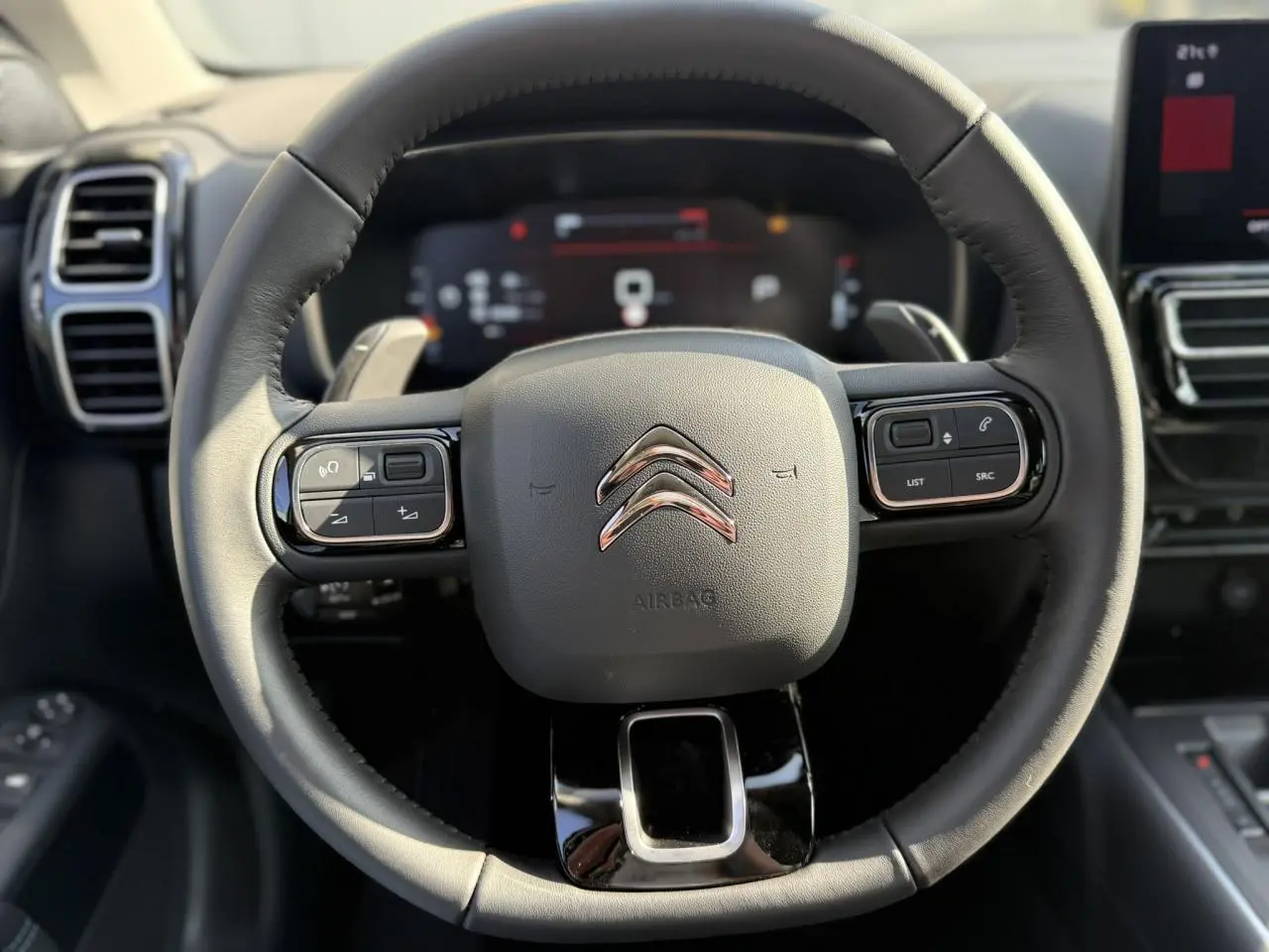 Vue rapprochée du volant noir en cuir du Citroën C5 Aircross 2025 avec commandes intégrées et tableau de bord numérique flou.