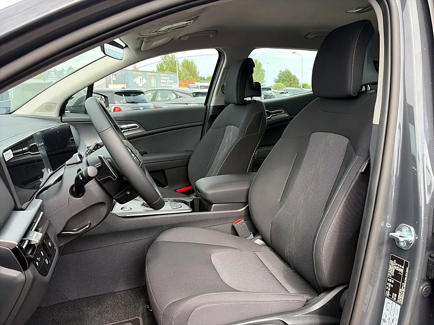 Vue intérieure côté conducteur du Kia Sportage 1.6 hybride gris eclipse, montrant sièges et volant multifonction cuir.