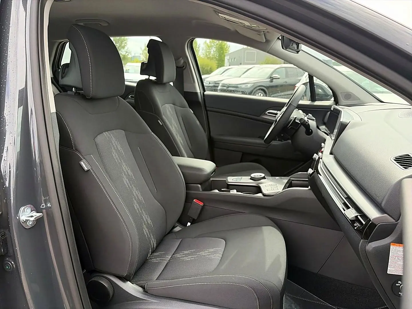 Vue intérieure côté conducteur du Kia Sportage 1.6 hybride gris eclipse, montrant sièges et console centrale moderne.