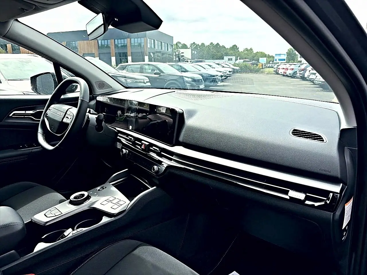 Vue intérieure côté conducteur du tableau de bord et console centrale du KIA Sportage 1.6 hybride gris eclipse 2026, volant cuir multifonction.
