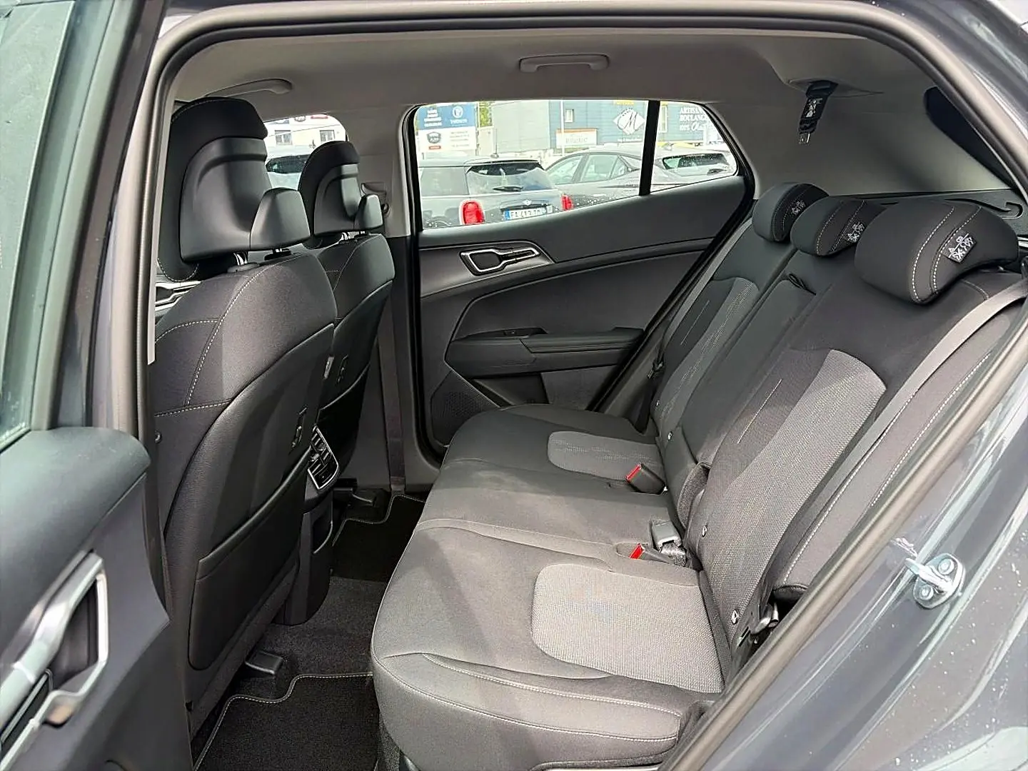 Vue intérieure côté droit de la banquette arrière grise du Kia Sportage 1.6 hybride 239 active avec appuie-têtes et porte ouvert.