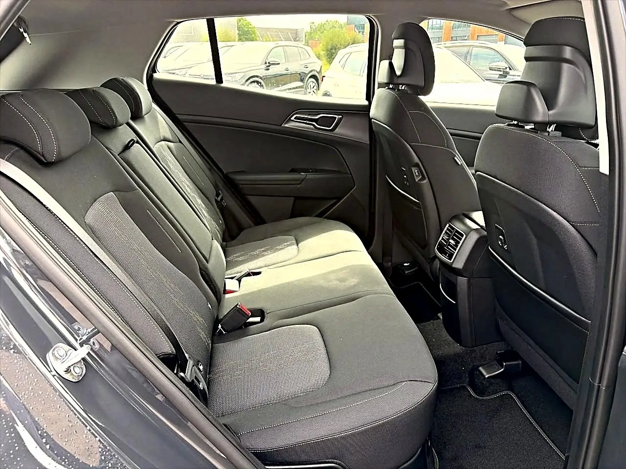 Vue intérieure côté gauche des sièges arrière gris foncé du Kia Sportage 1.6 hybride 239 active avec accoudoirs et aérateurs centraux.