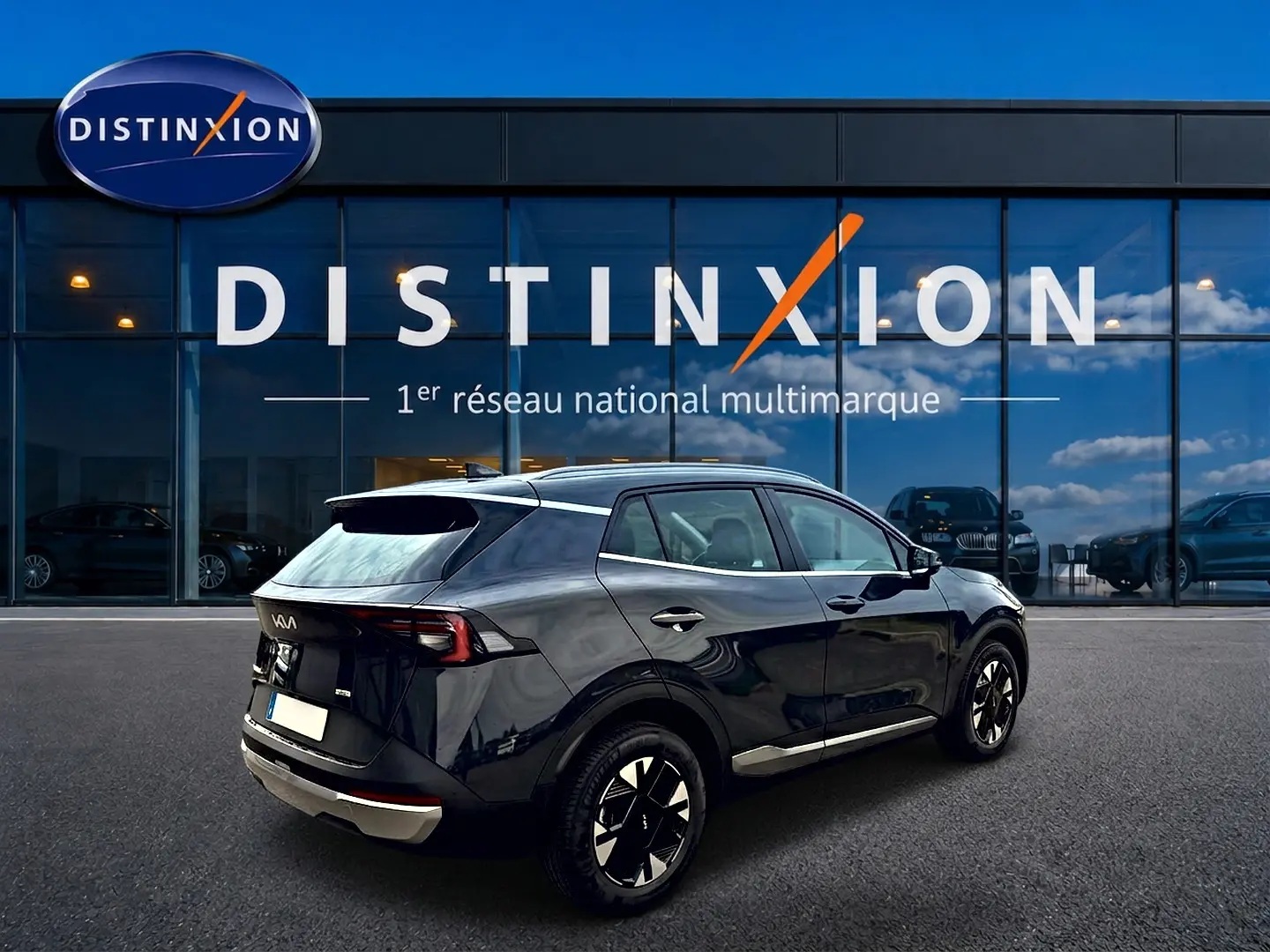 Vue 3/4 arrière droite d'un KIA SPORTAGE 1.6 hybride 239 gris eclipse avec jantes alu et feux arrière LED, devant un showroom Distinxion.