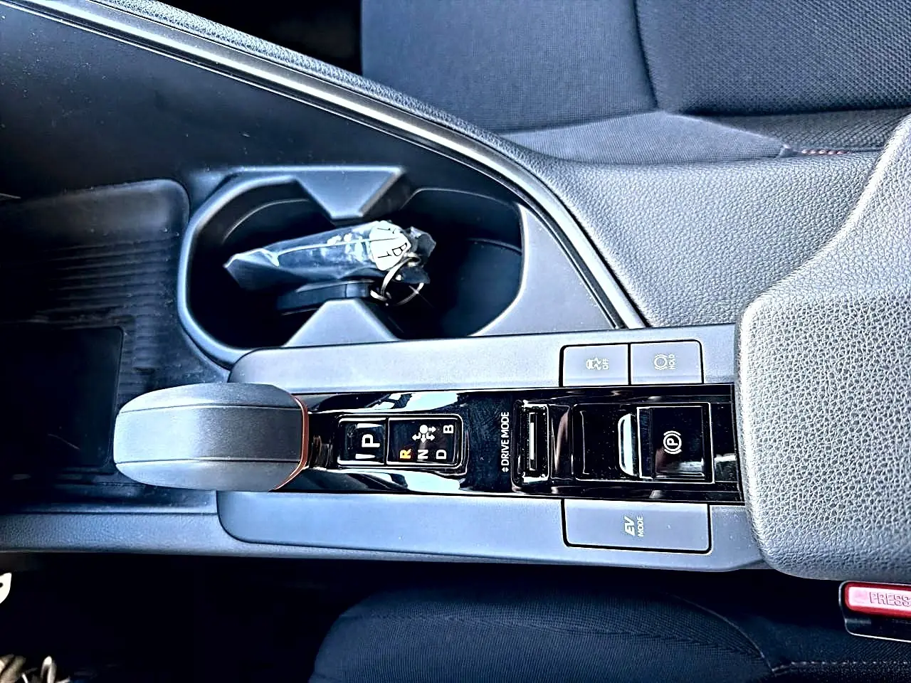 Vue plongeante sur la console centrale noire du Toyota C-HR gris, avec levier de vitesse automatique et accoudoir.