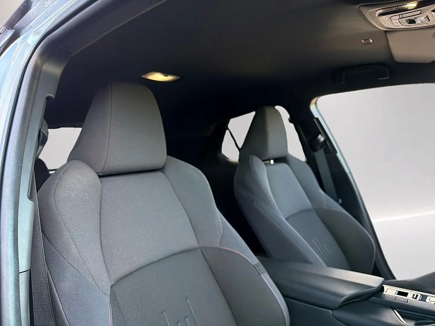 Vue intérieure des sièges avant en tissu gris foncé du Toyota C-HR 1.8 hybride 2025 avec accoudoir central.