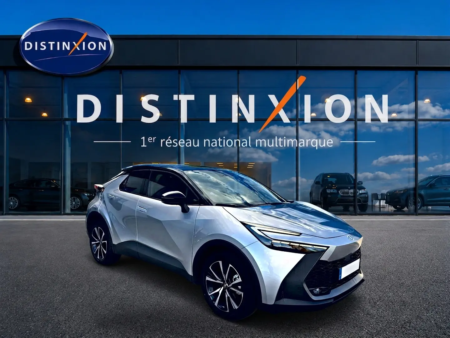 Toyota C-HR 1.8 hybride gris en 3/4 avant droit, avec jantes alu et calandre distinctive noire devant showroom Distinxion.