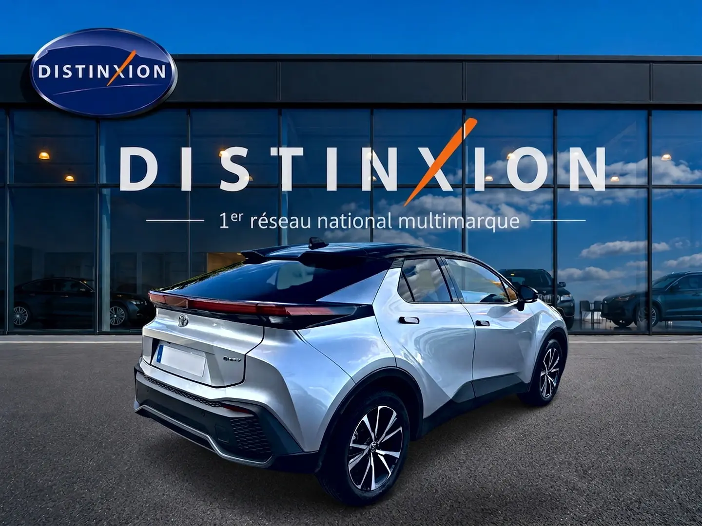 Toyota C-HR hybride gris en 3/4 arrière droit, avec toit noir et feux arrière LED continus, devant une vitrine Distinxion.