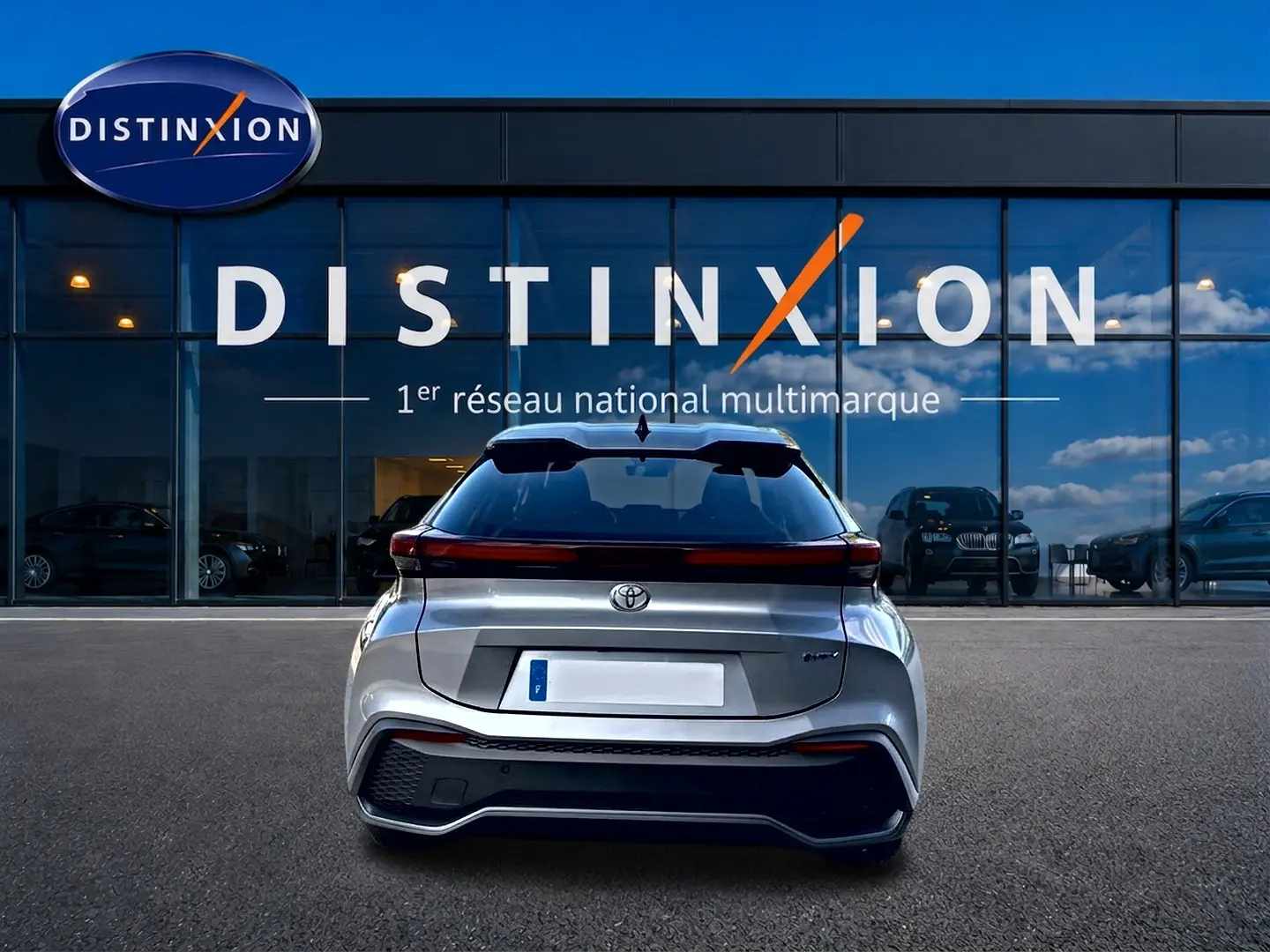 Vue arrière d'un Toyota C-HR gris 2025 hybride, avec feux arrière LED et logo Toyota visible devant une vitrine Distinxion.