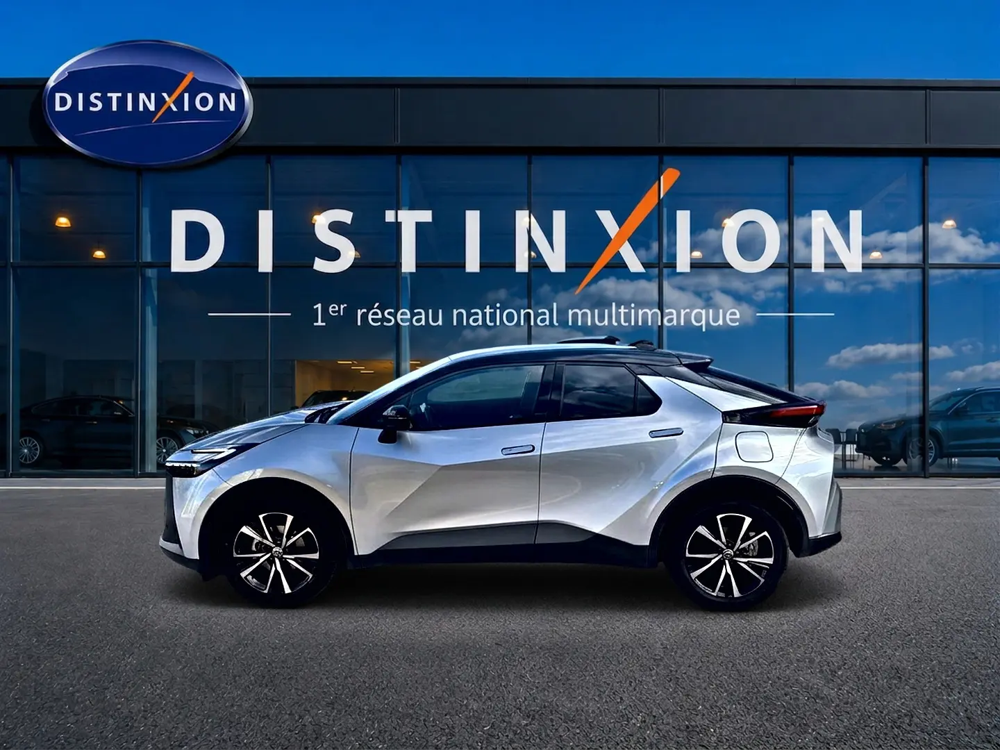 Toyota C-HR 1.8 hybride gris en profil droit devant une vitrine avec logo Distinxion en arrière-plan.