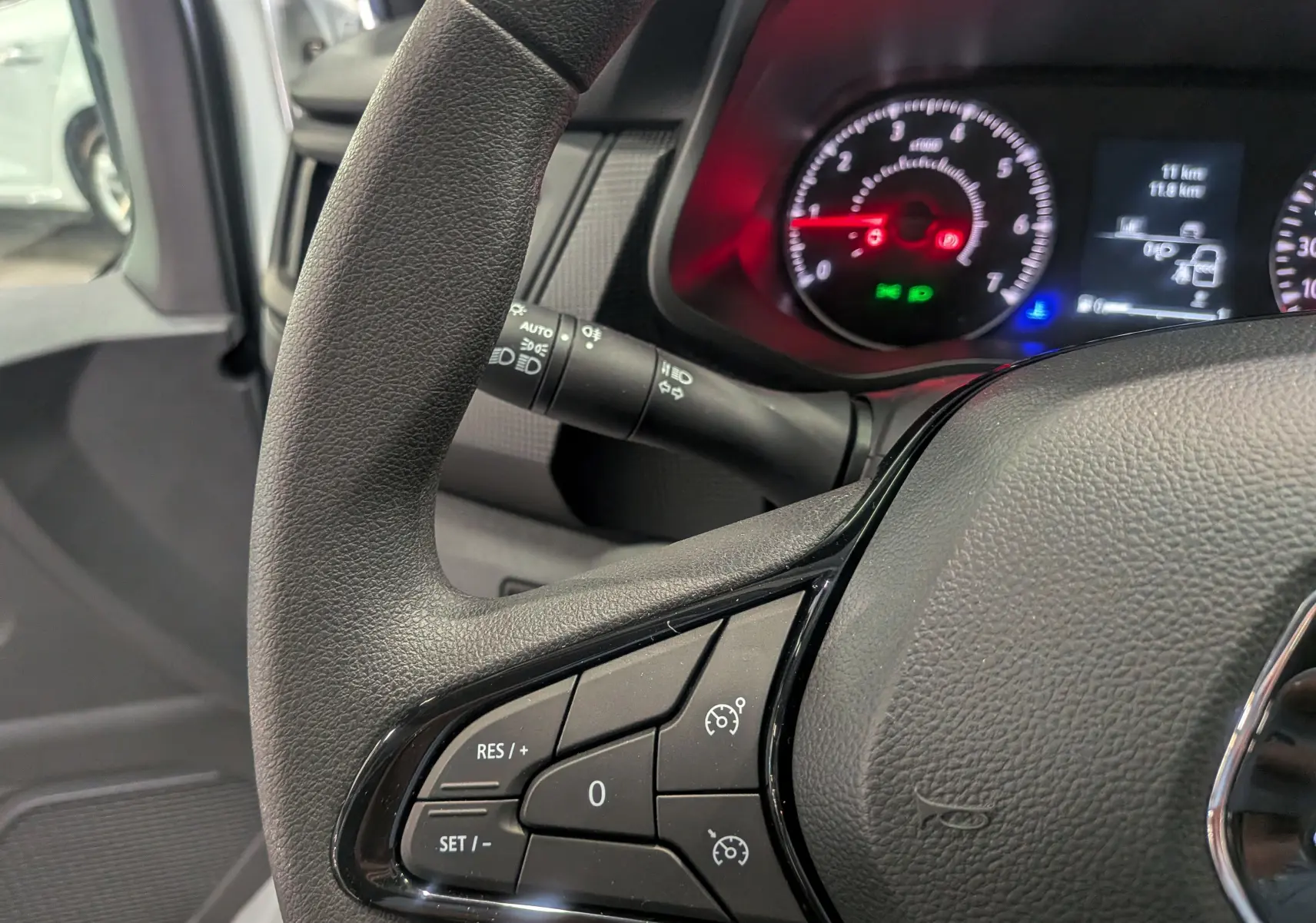 Gros plan sur le volant du Renault Trafic cabine approfondie 2023, montrant les commandes de régulateur de vitesse et le tableau de bord allumé.