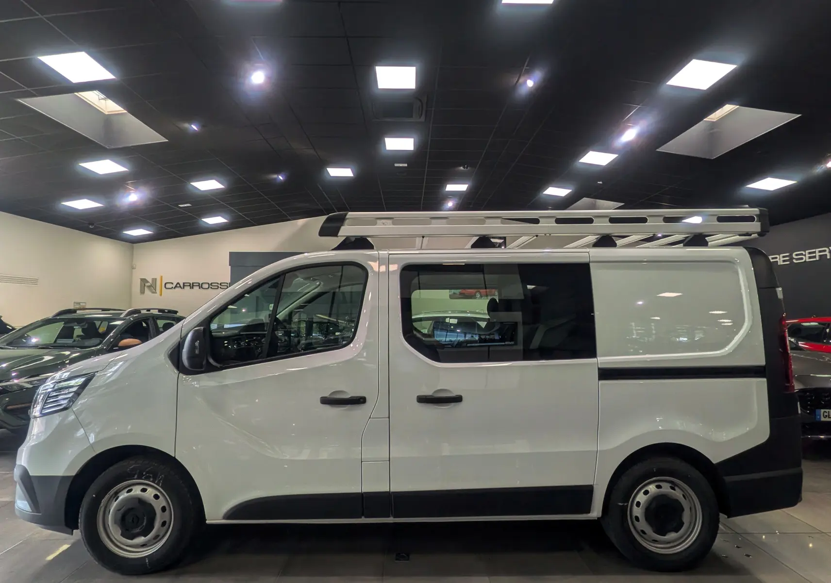 Vue de profil côté gauche du Renault Trafic Cabine Approfondie blanc minéral avec échelle sur le toit en intérieur showroom.