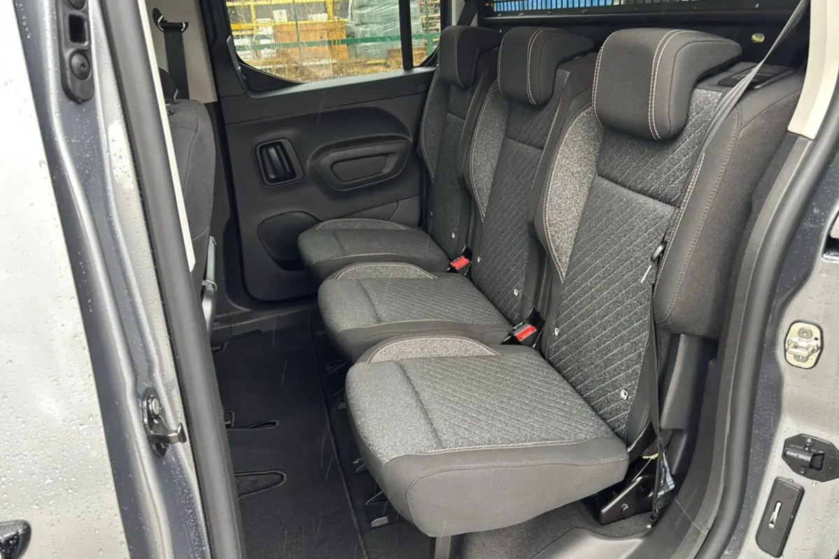 Vue intérieure côté droit sur la banquette arrière tissu gris du Peugeot Rifter 2026 gris artense avec porte ouverte.