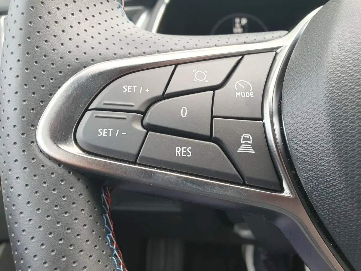 Gros plan sur les commandes au volant du Renault Captur 2026, boutons noirs avec surpiqûres tricolores sur cuir perforé.