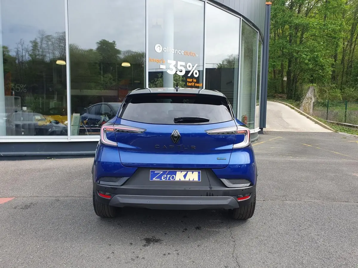 Vue arrière d’un Renault Captur bleu Iron 2026 avec feux LED et plaque Zero KM devant un bâtiment vitré.