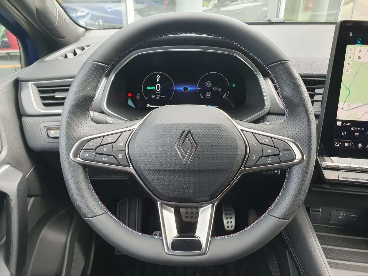 Vue rapprochée du volant noir perforé avec surpiqûres tricolores du Renault Captur 2026, tableau de bord numérique et écran tactile visible.