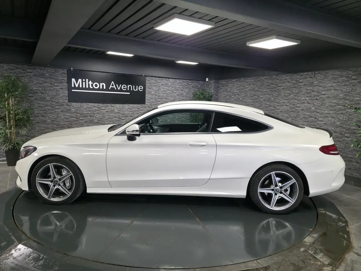 Vue latérale droite d'une Mercedes Classe C Coupé blanc nacré avec jantes alliage AMG à 5 branches dans un showroom.