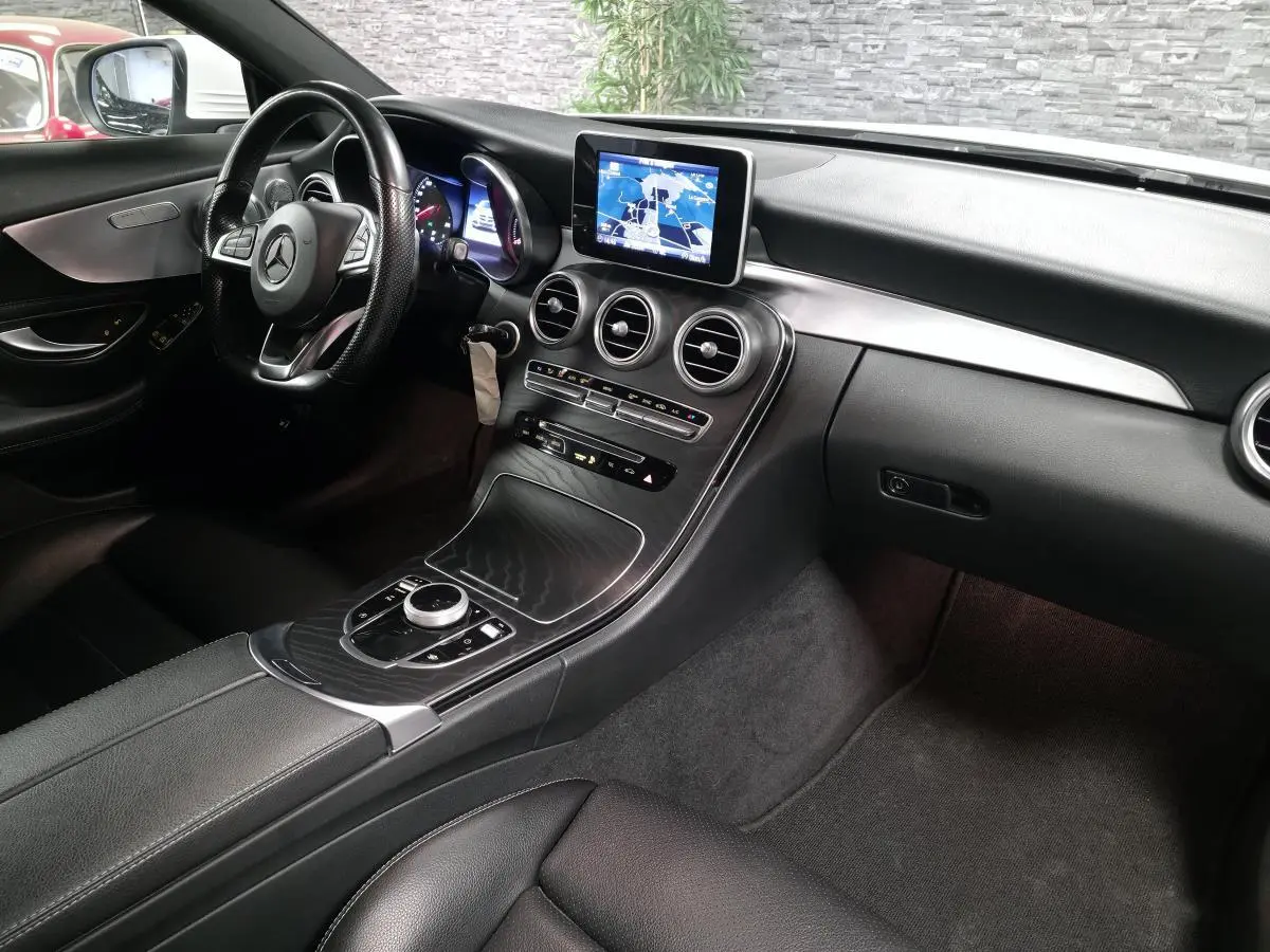 Vue intérieure côté conducteur du tableau de bord noir et console centrale avec écran GPS de la Mercedes Classe C Coupé blanc.