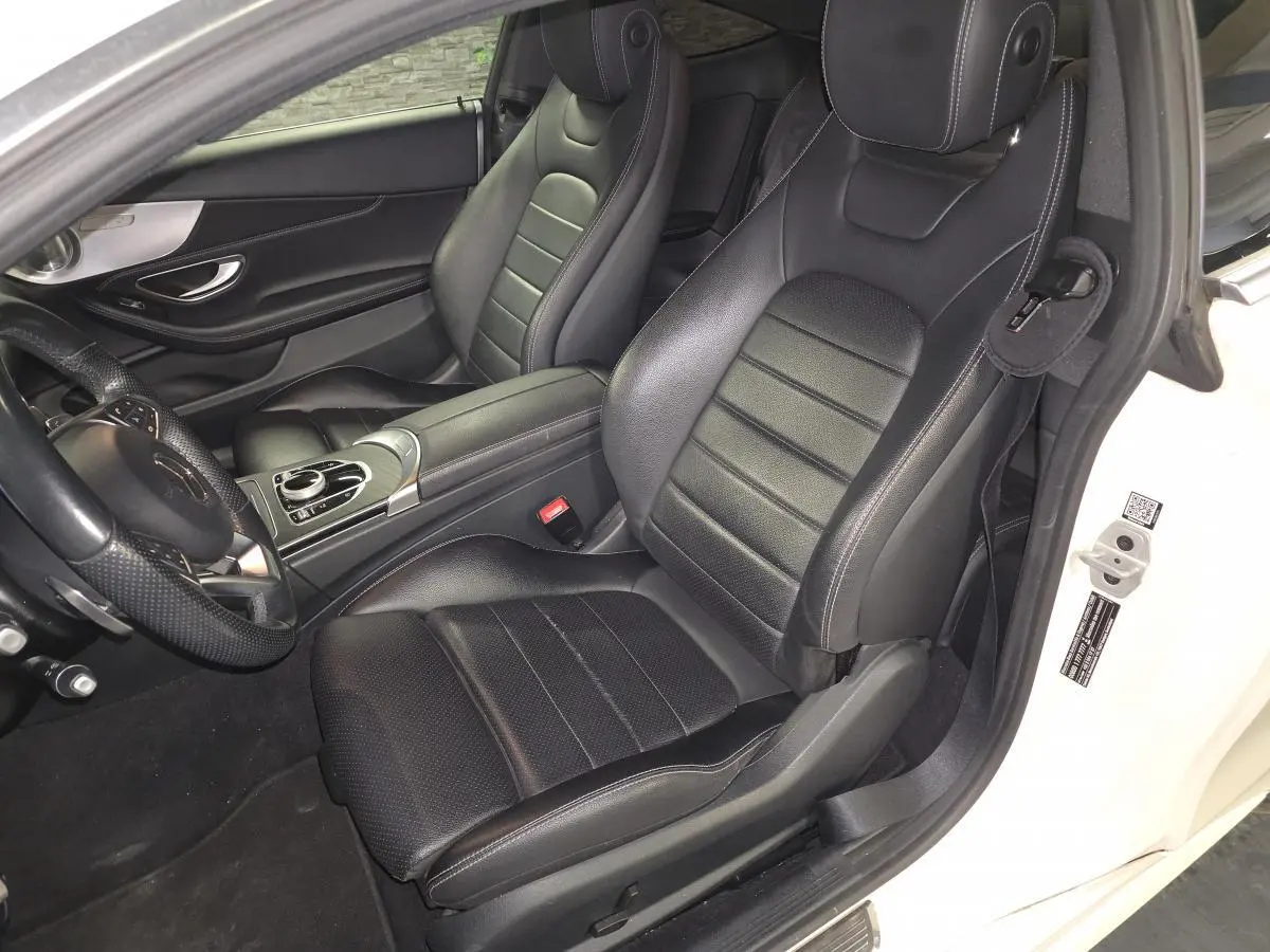 Vue intérieure côté conducteur d'un Mercedes Classe C Coupé blanc, sièges sport en cuir noir avec surpiqûres grises.