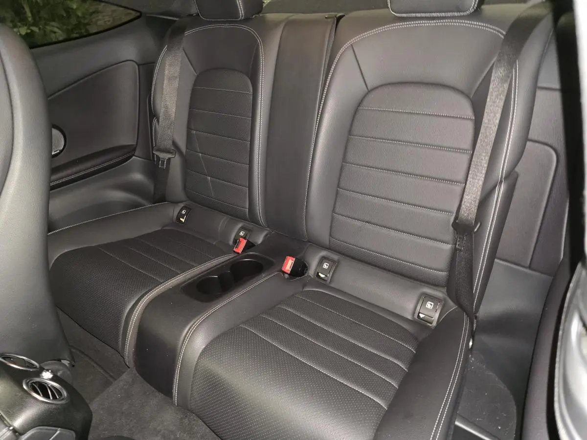 Vue intérieure sur la banquette arrière noire en similicuir avec ceintures et accoudoir central de la Mercedes Classe C Coupé.