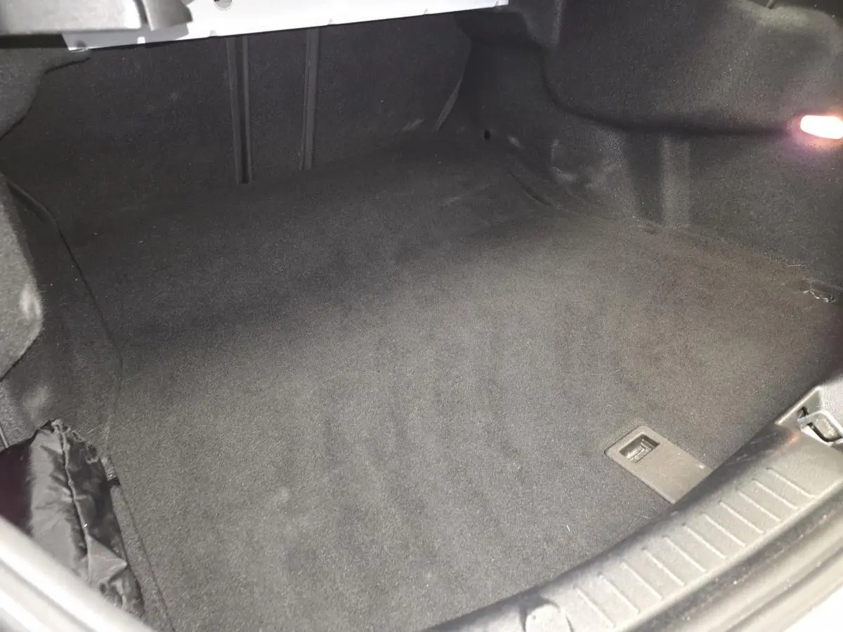 Coffre ouvert de Mercedes Classe C Coupé blanc, vue intérieure montrant le tapis noir et l'éclairage latéral.