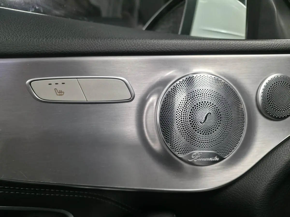 Détail intérieur côté porte avec bouton de siège chauffant et haut-parleur Burmester en finition aluminium brossé.