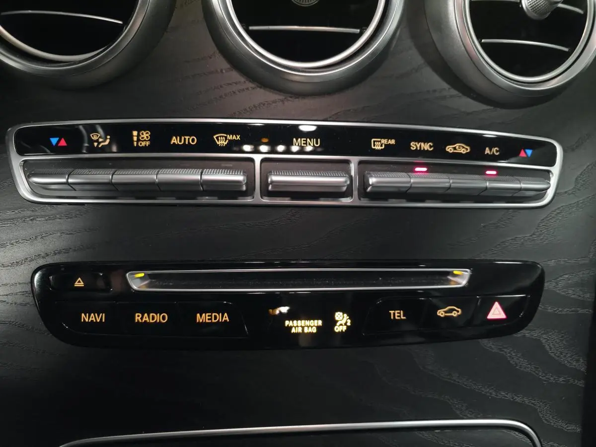 Vue rapprochée de la console centrale noire avec commandes climatisation et multimédia d'une Mercedes Classe C Coupé blanc.
