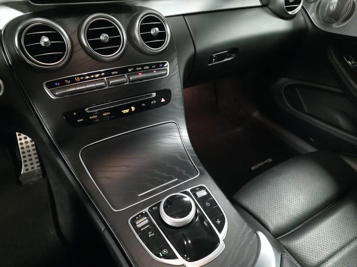 Vue intérieure côté passager du tableau de bord et console centrale noire avec commandes multimédia et aérateurs ronds Mercedes AMG.