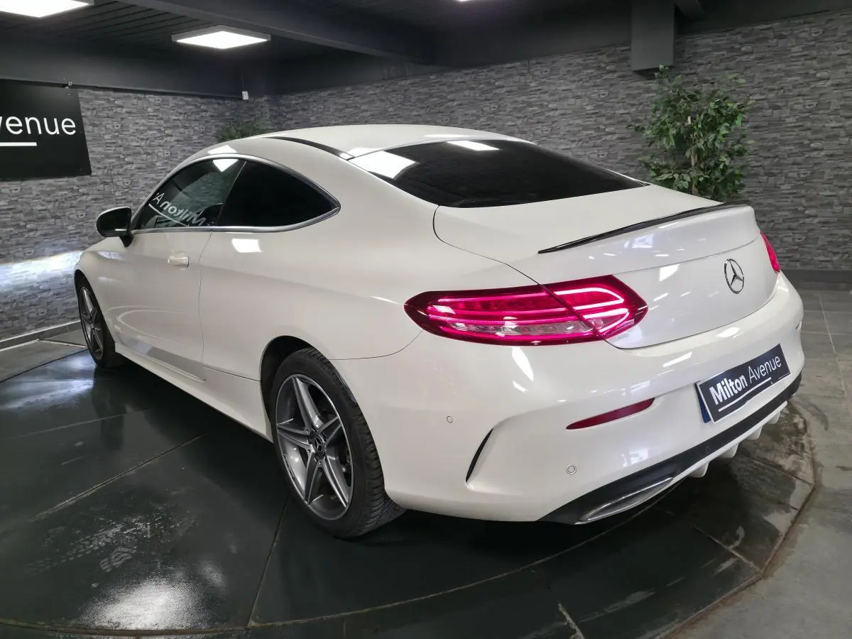 Vue 3/4 arrière droite d'une Mercedes Classe C Coupé blanc avec jantes AMG 5 branches et feux arrière LED allumés.