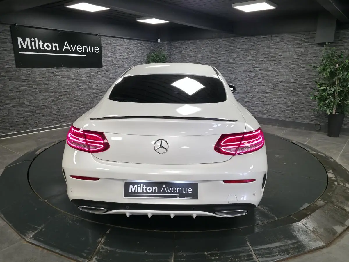 Vue arrière d'un Mercedes Classe C Coupé blanc avec feux LED allumés et double sortie d'échappement chromée.