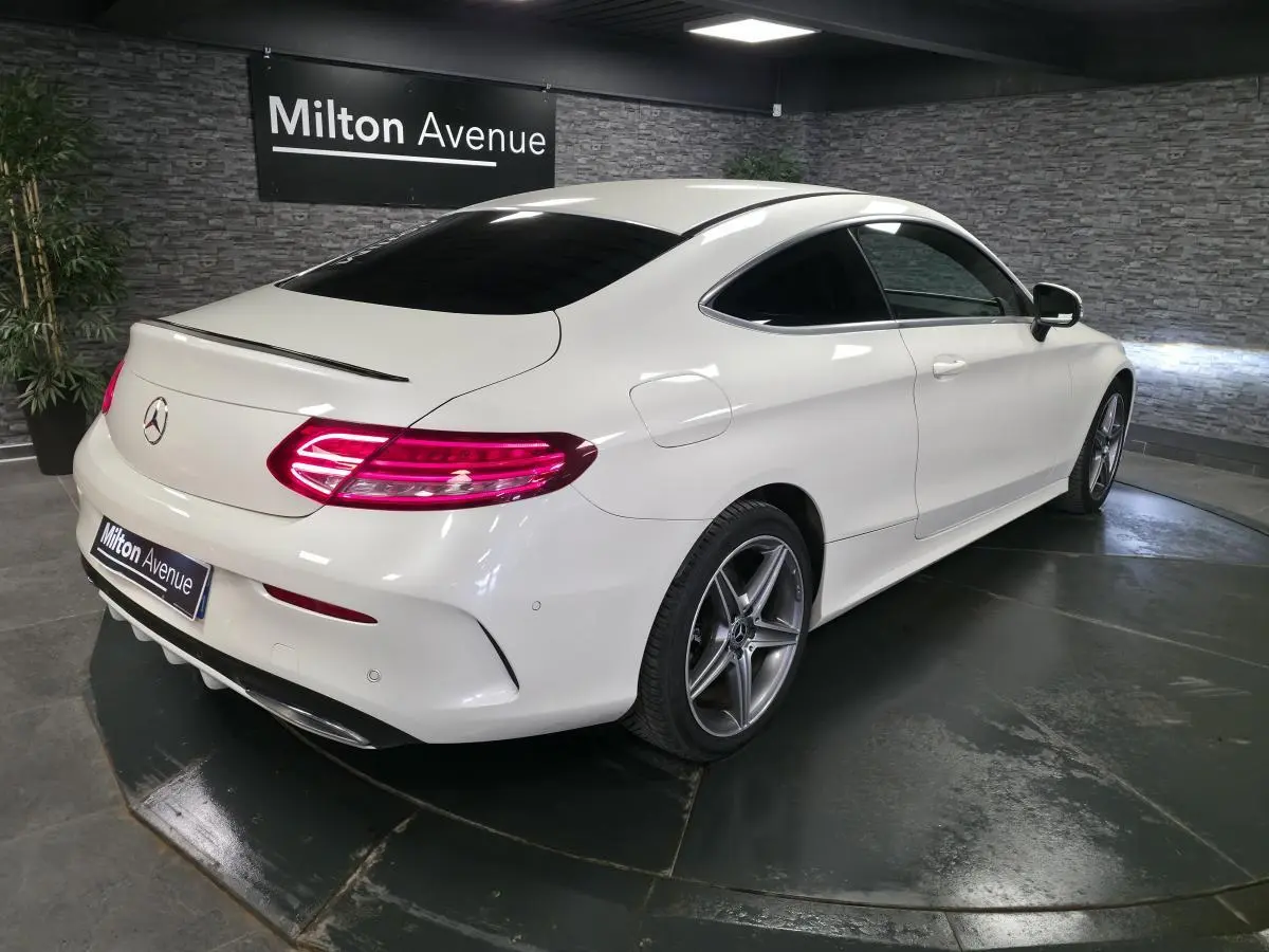 Mercedes Classe C Coupé blanc vue 3/4 arrière droit, jantes AMG 5 branches et feux arrière LED allumés.
