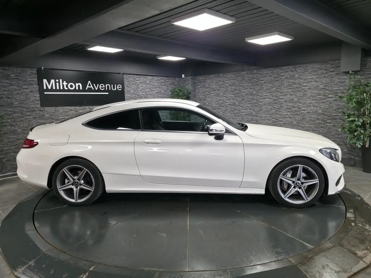 Vue latérale droite d'un coupé Mercedes Classe C blanc avec jantes alliage AMG 5 branches dans un showroom.