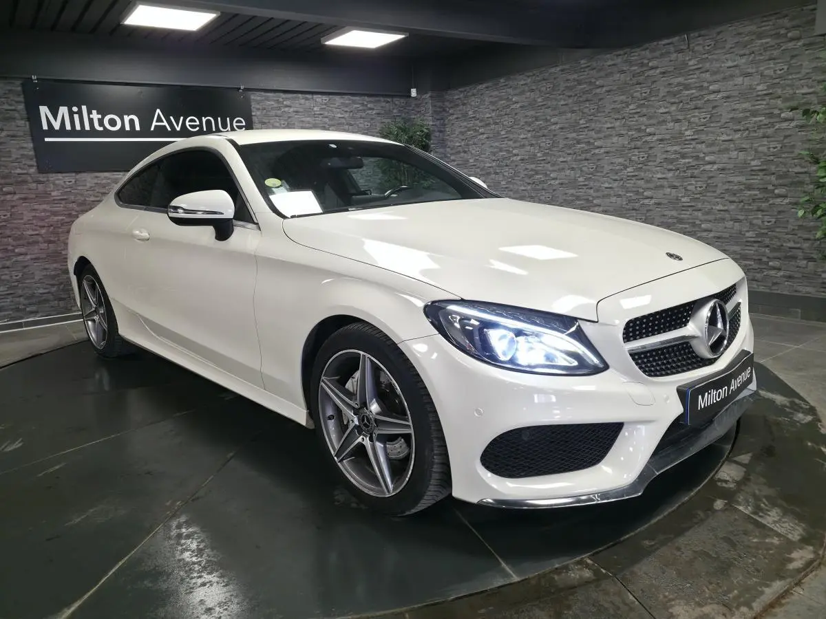 Mercedes Classe C Coupé blanc vu en 3/4 avant droit, avec jantes AMG 5 branches et phares LED allumés.