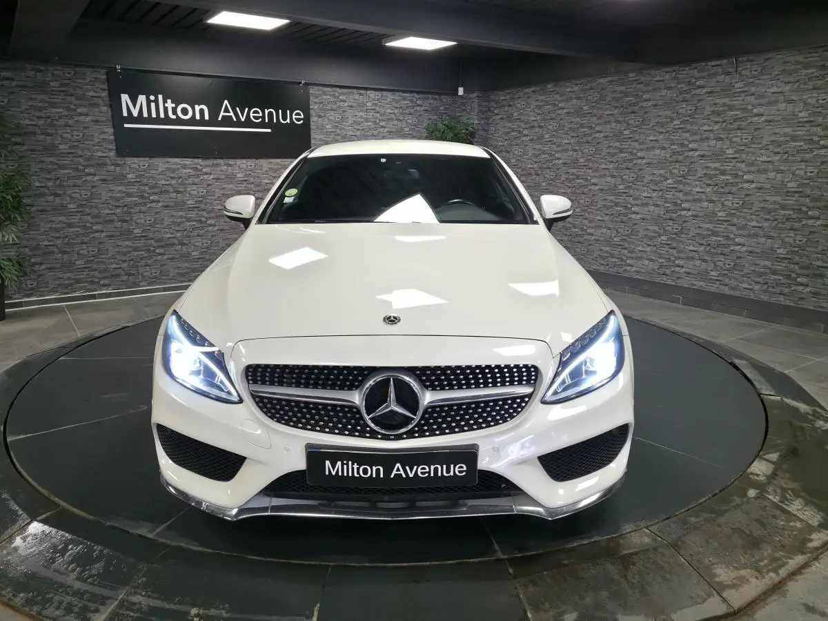 Vue avant d'une Mercedes Classe C Coupé blanc avec calandre AMG et phares LED allumés en showroom.