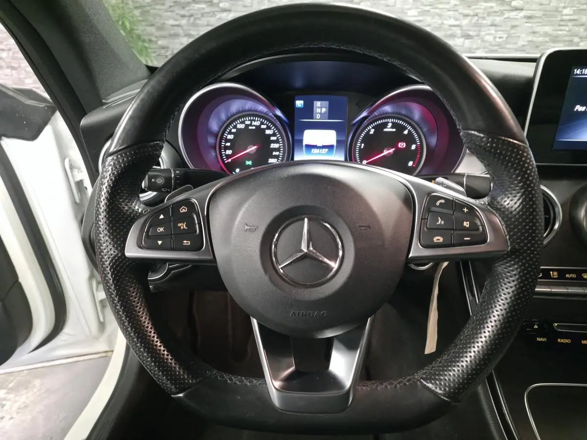Vue rapprochée du volant sport en cuir noir perforé d’une Mercedes Classe C Coupé blanc, avec tableau de bord digital allumé.