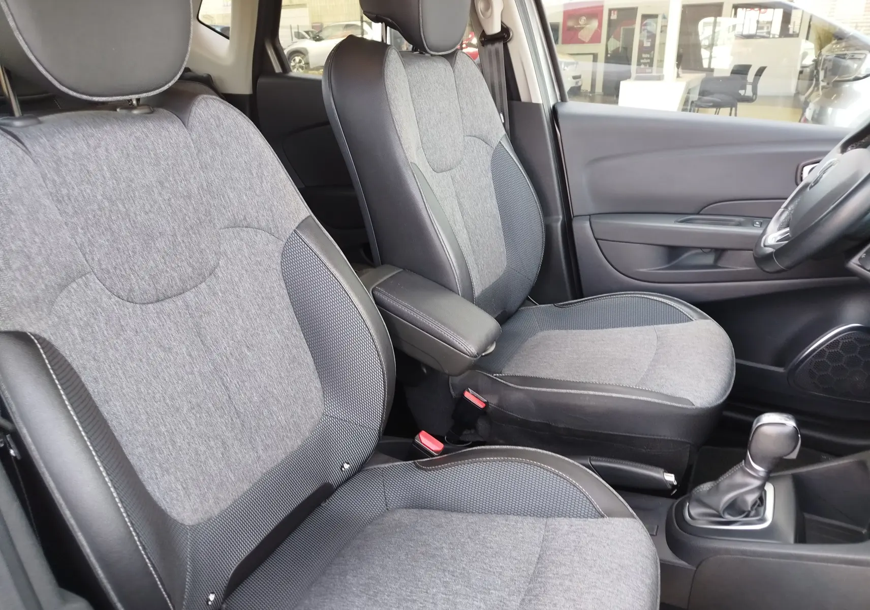 Vue intérieure côté droit des sièges avant gris clair et foncé du Renault Captur avec accoudoir central et levier de vitesses automatique.