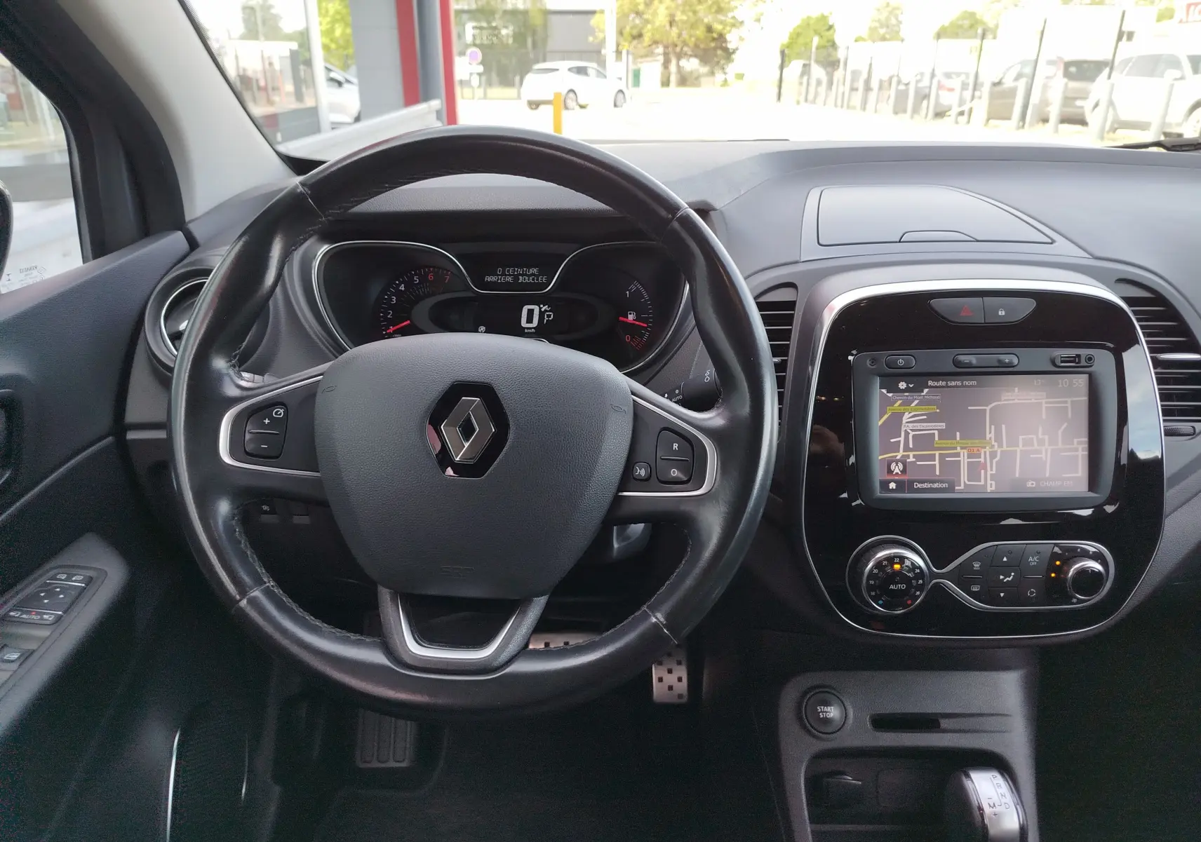 Vue intérieure du tableau de bord du Renault Captur gris, avec volant, écran tactile et commandes de climatisation visibles.