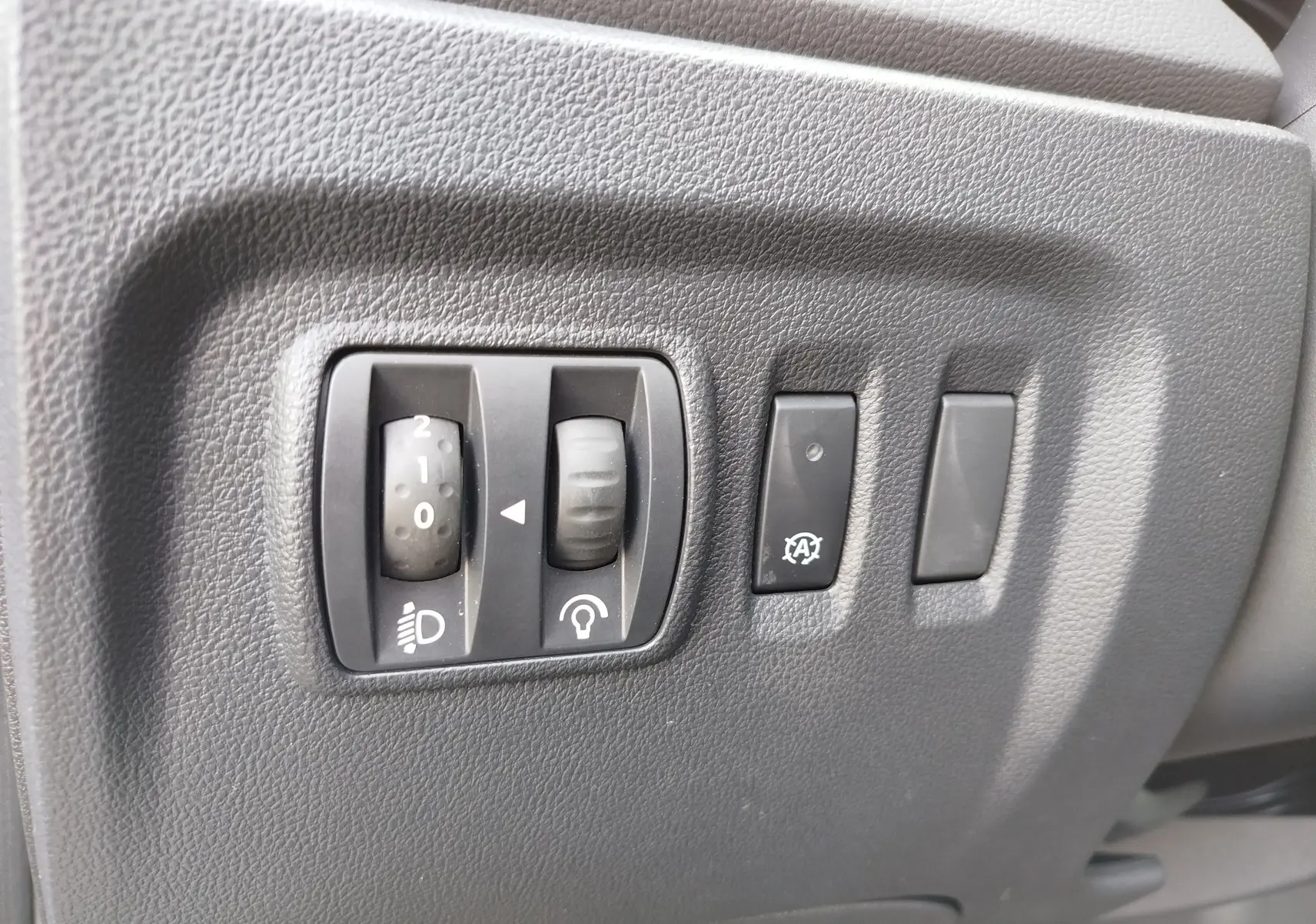 Gros plan sur les commandes de réglage des phares et du tableau de bord, intérieur noir du Renault Captur Gris Cassiopée.