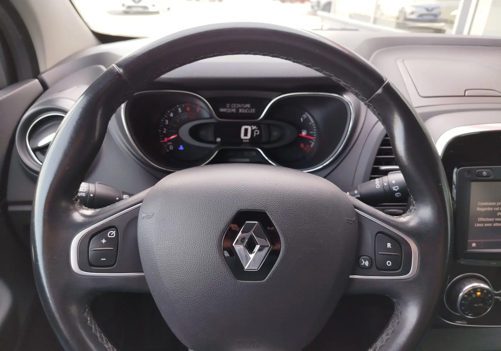 Vue intérieure centrée sur le volant à droite et la console centrale du Renault Captur gris Cassiopée, version 2018.