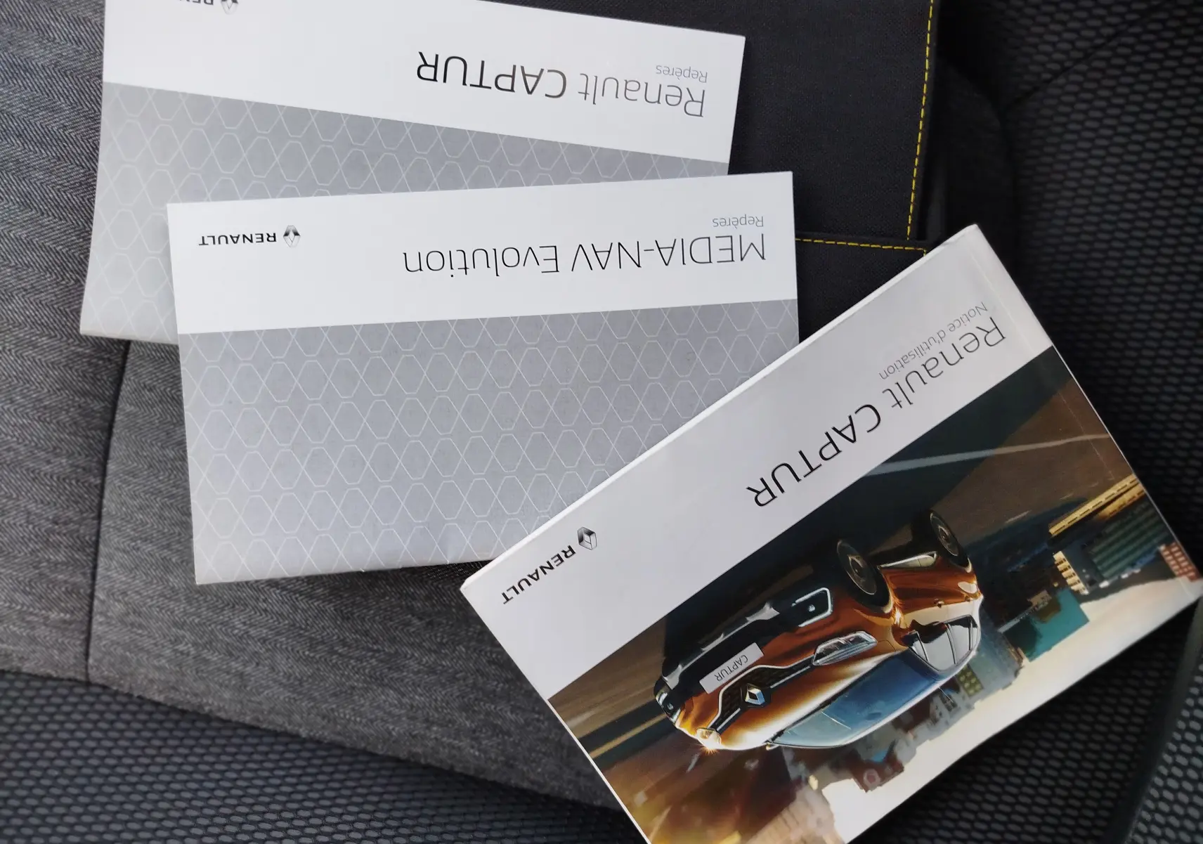 Brochures Renault Captur posées sur un siège, couverture montrant un Captur orange en 3/4 avant dans un décor urbain.