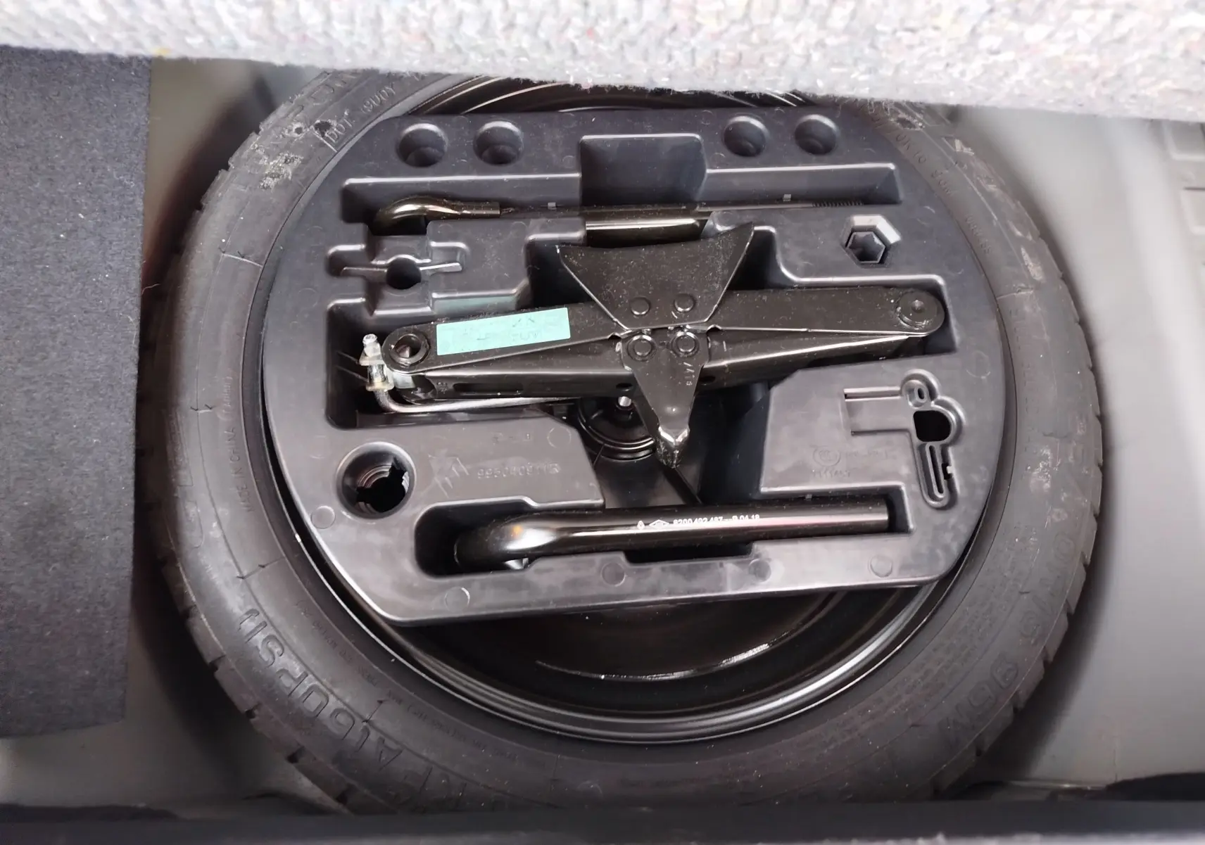 Roue de secours avec cric et outils rangés dans le coffre d’un Renault Captur Gris Cassiopée, vue de dessus.