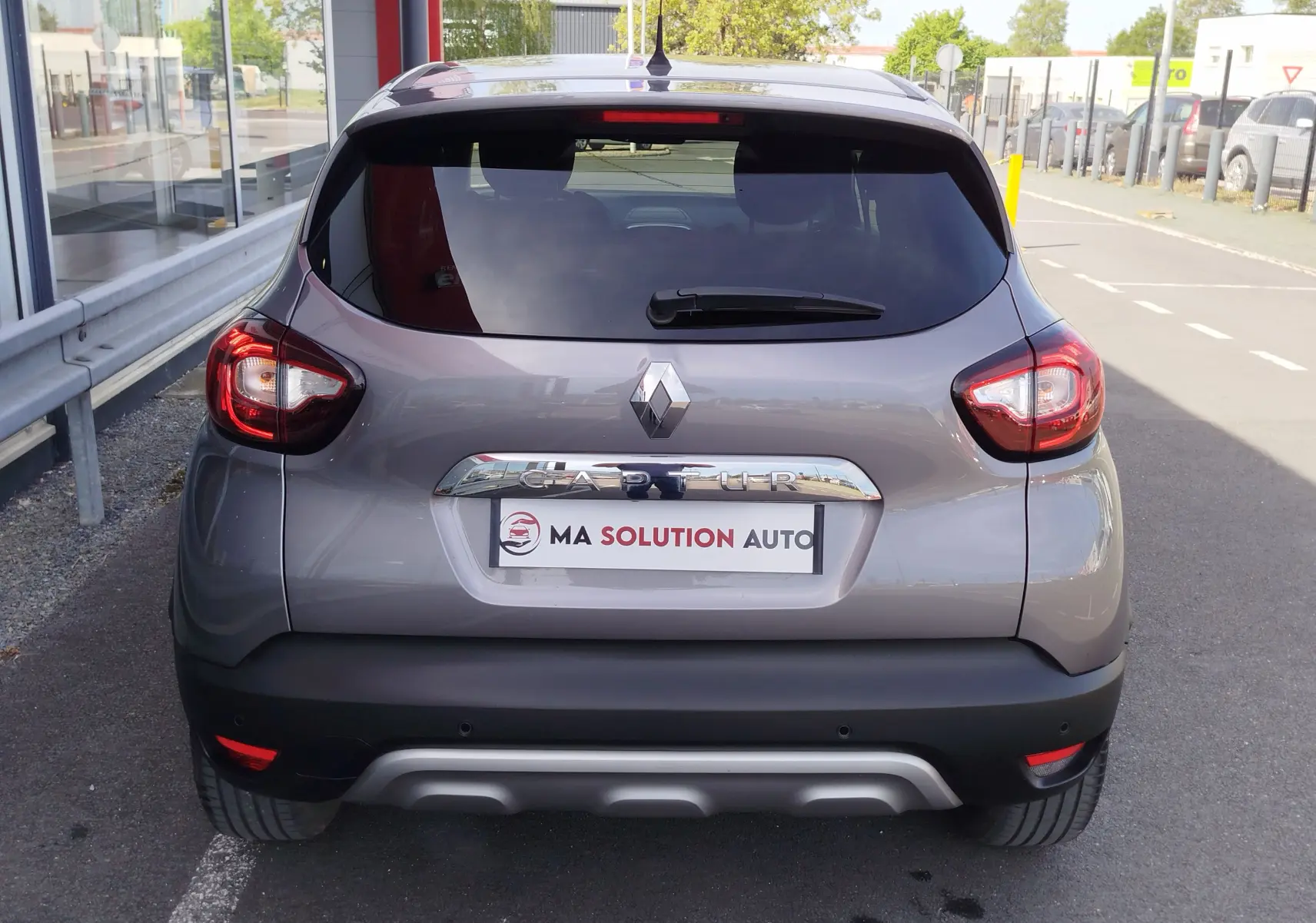Vue arrière d'un Renault Captur gris Cassiopée 2018 avec feux LED et logo chromé distinctif sur un parking urbain.
