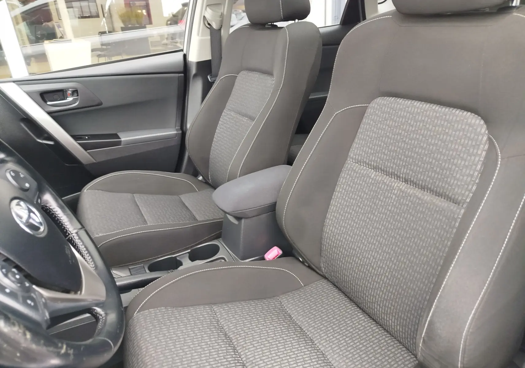 Vue intérieure côté conducteur de la Toyota Auris HSD 136h 2015, sièges tissu gris avec surpiqûres blanches.