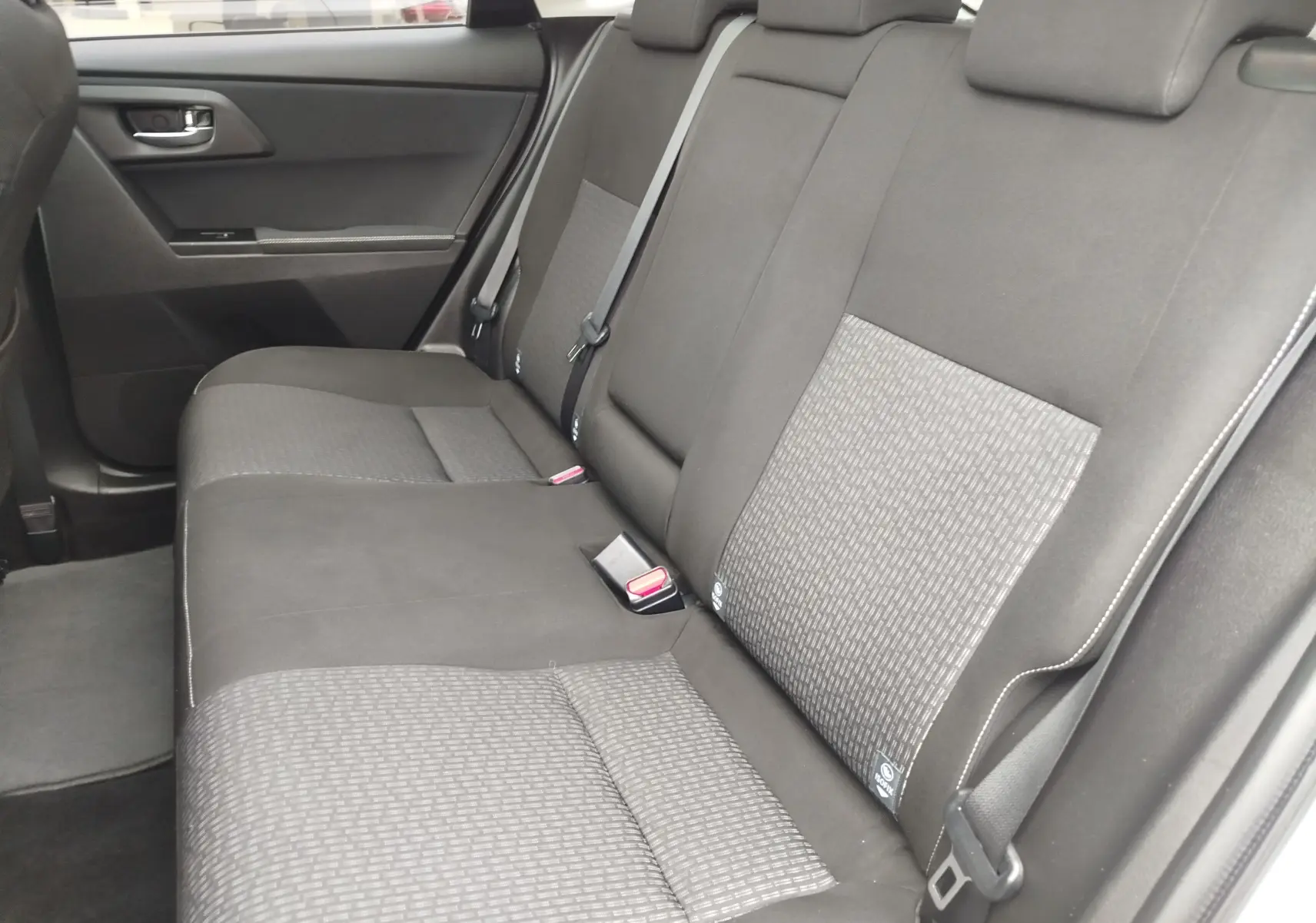 Vue intérieure des sièges arrière gris foncé de la Toyota Auris HSD 136h SkyBlue, avec ceinture de sécurité et porte côté gauche visible.