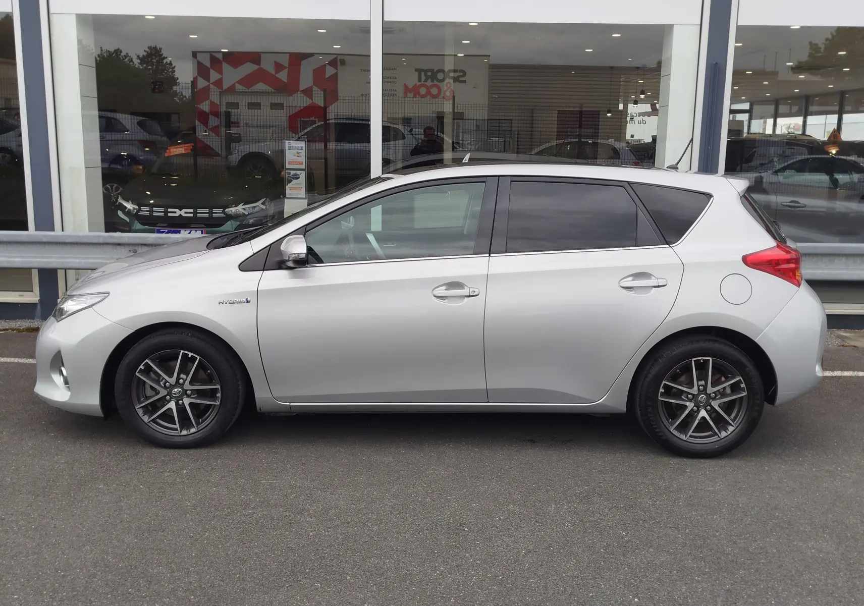 Profil droit d'une Toyota Auris HSD 136h gris aluminium de 2015, avec jantes alliage et vitres teintées.